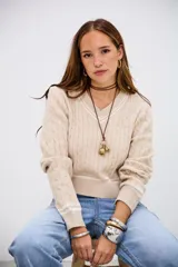 Sweater de punto trenzado en color beige, con cuello en V y detalles de rayas blancas en el cuello, puños y ruedo. De corte ajustado y manga larga.