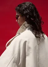 Chaqueta larga de algodón color beige, de diseño recto con cuello en pico y solapas con muesca. Cuenta con cierre delantero de doble botonadura, bolsillos laterales y mangas largas reversibles.