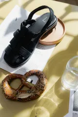 Sandalias de cuero negro con diseño de tiras entrelazadas, estilo huarache, con pulsera ajustable al tobillo mediante hebilla metálica.