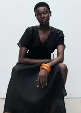 Vestido largo de color negro con cuello en pico y mangas cortas. Presenta un panel fruncido en la cintura que define la silueta y un diseño recto. Confeccionado en una mezcla de lino y ramio con forro de algodón.