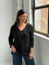 Blusa negra de manga larga con escote en V y costuras decorativas en color blanco. Presenta un corte holgado con aberturas laterales en el ruedo.