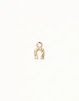 Dije de metal dorado con forma de herradura y pequeños detalles calados. Incluye aro superior para colgar en cadenas o pulseras.