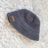 Gorro tipo bucket de sherpa color gris con etiqueta de cuero sintético con logo de la marca.