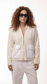 Campera de corte relajado color crema, con cierre frontal completo y cuello tipo bomber. Presenta dos bolsillos frontales destacados con apliques de lentejuelas blancas.