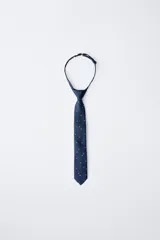 Corbata azul marino con estampado de pequeños topos blancos, cuenta con un sistema de cierre ajustable en la nuca.