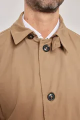 Gabardina color beige de algodón, con cuello clásico, cierre frontal con botones, dos bolsillos de ribete delanteros, bolsillo interior con botón y abertura posterior en el bajo.