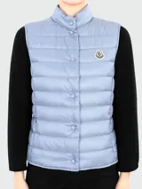 Chaleco acolchado Moncler modelo Liane, color celeste, con cierre frontal de botones a presión, cuello alto y logo de la marca aplicado en el pecho.