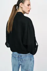 Blusa negra de cuello solapa y manga corta, con bolsillos con solapa en el pecho, bajo elástico y cierre frontal con botones.