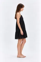 Vestido corto negro de algodón con diseño holgado, escote cuadrado y tirantes finos. Presenta detalles de bordado con perforaciones en toda la prenda y falda con volados en capas.