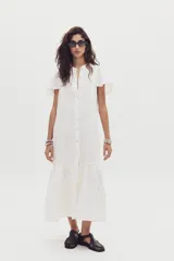 Vestido midi de lino color blanco, con cuello mao, cierre frontal con botones y mangas cortas con volados. Presenta un diseño holgado con un volado en el ruedo.