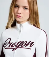Campera deportiva de corte ajustado, color blanco con paneles laterales y detalles en mangas color bordó. Presenta cierre frontal completo, cuello alto y estampa con lettering 'Oregon' en el pecho.