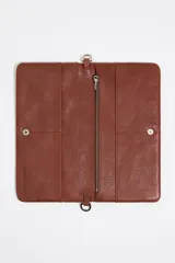 Minibolso negro de piel vacuna con textura granulada, formato rectangular y cierre de botón a presión. Incluye un tarjetero interior y dos asas: una de mano tipo cordón trenzado rojo y naranja, y una asa larga extraíble.