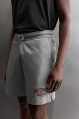 Pantalones cortos de algodón color gris, con cintura elástica ajustable con cordón y parche con logo. Incluye bolsillos laterales y un bolsillo trasero. Presenta bandas laterales a tono, bordado y estampado combinado a contraste en el delantero y la espalda, y aberturas laterales en el bajo.