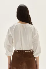 Blusa de algodón de corte holgado, con cuello redondo fruncido y cierre de lazo frontal. Presenta mangas largas con puños elásticos.