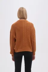 Sweater de tejido de punto color verde oliva, con cuello redondo y manga larga. Presenta un diseño de punto trenzado en el frente y mangas, contrastando con un tejido acanalado liso en el lado derecho del torso.