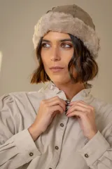 Gorro tipo ushanka de cuero con interior y borde de piel sintética afelpada en tono beige.