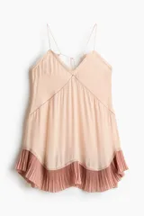 Vestido corto de corte holgado en crepé rosado claro, con escote en V pronunciado adelante y atrás, y breteles finos que se entrelazan en la espalda. Presenta un volado plisado en el borde inferior en un tono rosado más oscuro.