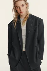 Blazer oversize de corte recto con cuello de solapa, manga larga con hombreras y cierre frontal de doble botonadura. Presenta un diseño en color gris oscuro con costuras decorativas a contraste en color blanco, bolsillos con solapa y forro interior.