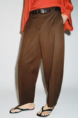Pantalón tiro bajo color marrón, de corte globo y pernera recta con raya marcada al frente. Incluye trabillas y un cinturón marrón oscuro con hebilla metálica.