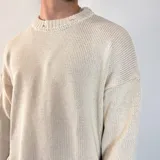Sweater tejido color crudo, de corte holgado, con cuello redondo y terminaciones rotas en puños y ruedo.