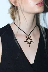 Collar de cordón negro con dije metálico plateado en forma de sol con diseño irregular y estilo gótico.