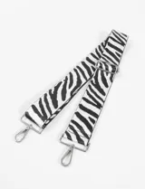 Correa de tela blanca con estampado de cebra en negro, con herrajes metálicos plateados y mosquetones en los extremos.