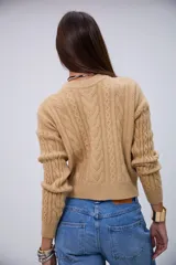 Sweater de punto color beige con cuello redondo, mangas largas y detalles de trenzas en el frente y las mangas.