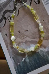 Gargantilla corta con cuentas de piedra irregulares en tonos amarillo pálido y beige, combinadas con cuentas facetadas rectangulares. Incluye un segundo collar con eslabones grandes dorados y un dije con forma de herradura dorada.