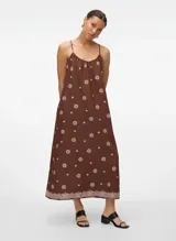 Vestido largo marrón con tirantes finos y escote cuadrado. Presenta un estampado repetido de círculos y pequeñas flores en color beige claro, con un borde de encaje o puntilla en el ruedo.