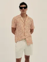 Camisa de manga corta con cuello estilo cubano y estampado de manchas color naranja sobre fondo blanco.