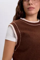Chaleco de punto estilo varsity color marrón, con cuello redondo y detalles de rib en color beige claro en los bordes y sisas.