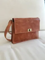 Cartera bandolera de cuero marrón con solapa frontal, cierre metálico de giro y correa ajustable.