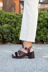 Sandalias de cuero color marrón chocolate con taco ancho, diseño de tiras cruzadas con textura símil serpiente y tira ajustable en el talón con hebilla metálica.