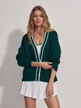 Cárdigan de punto verde oscuro con cuello en V y botones. Presenta ribetes blancos en el cuello, el frente y los puños.