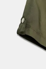 Vestido corto de estilo utilitario en color verde militar, confeccionado en gabardina. Presenta cuello redondo, cierre frontal con cremallera oculta, mangas cortas con detalle de trabilla y botón, y bolsillos de plastrón en el frente.