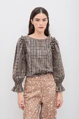Blusa de manga larga con estampado a cuadros en tonos marrones y grises. Presenta un diseño con volados en los hombros, mangas abullonadas y puños elásticos con terminación de volado.