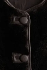 Chaleco de mujer confeccionado en tejido suave con efecto de pelo en color marrón oscuro. El diseño cuenta con cuello redondo, cierre frontal mediante botones a presión y prácticos bolsillos laterales discretos. Incluye forro interior y terminaciones con detalles revestidos.