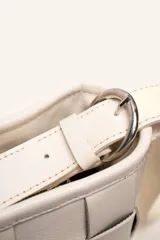 Cartera tipo morral de cuero color beige, con diseño trenzado artesanal, correa larga regulable y cierre superior.
