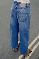 Jeans de tiro medio con cinco bolsillos, pernera holgada y diseño barrel, con costuras decorativas frontales y cierre de cremallera y botón.