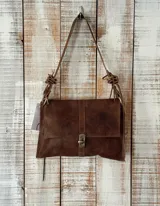 Cartera bandolera de gamuza color marrón oscuro, con solapa frontal y cierre metálico de gancho. Cuenta con una tira ajustable con nudos decorativos en los laterales.