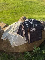 Polo de manga corta con cuello tipo polo y escote en V, corte boxy fit. Presenta un patrón texturizado en relieve y un logo ovalado con la inscripción "with love" en el pecho.