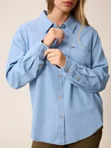 Camisa de jean de manga larga con cuello clásico, cierre frontal con botones y bolsillo en el pecho.