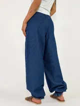 Pantalón de denim azul de corte holgado, tiro medio y diseño wide leg con puños fruncidos ajustables en los tobillos. Cuenta con bolsillos laterales y costuras decorativas.