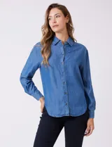 Camisa de tencel azul, marca Weekend Routine, con cuello solapa, botones metálicos frontales y manga larga regulable con presilla y botón. Presenta canesú horizontal en la espalda con tablón central y bajo asimétrico redondeado.