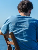 Remera blanca de manga corta con estampa en la espalda en color azul que incluye la frase 'Bo, hay pique!' y dibujos de peces y una caña de pescar.