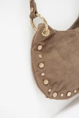 Cartera de hombro tipo baguette confeccionada en cuero gamuzado color camel, con detalle de tachas metálicas doradas en el contorno y correa fija.