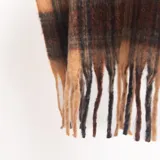 Mantón con diseño de cuadros en tonos tostados y marrones, adornado con flecos largos en los extremos.