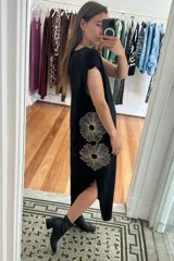 Vestido largo de color negro, con corte holgado, mangas cortas y tajo lateral. Presenta un diseño bordado de dos flores grandes en el lateral de la falda.