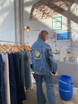 Campera de jean celeste con corte oversize, cuello camisero, cierre con botones metálicos y bolsillos frontales. Estampado en la espalda con un sol sonriente y la inscripción "Dos Orientales".