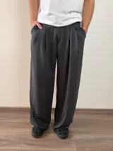 Pantalón de vestir de corte baggy, color gris oscuro, con pinzas frontales y bolsillos laterales.